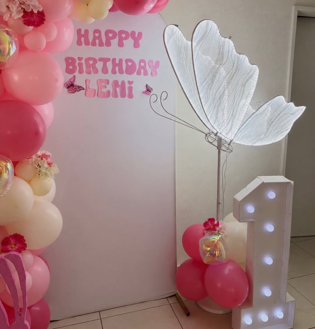 Beleuchteter Schmetterling neben Ballons in Rosa und einer Leuchtzahl 1